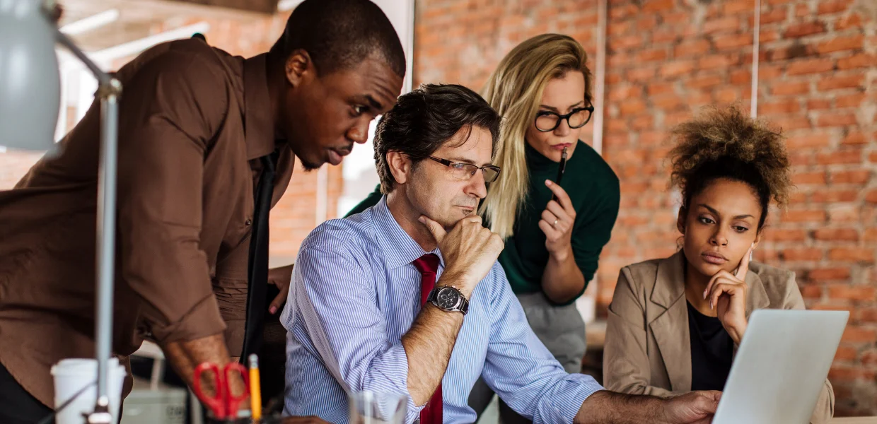 Diverse team of professionals collaborating around a laptop in a modern office during a change management discussion