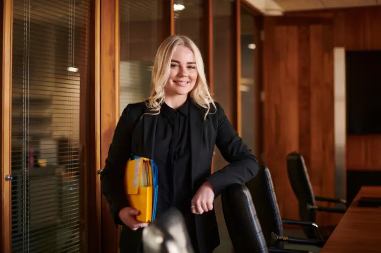 A young woman with blonde hair in a dark outfit seated in a professional environment, representing a graduate finding career clarity through self-awareness.